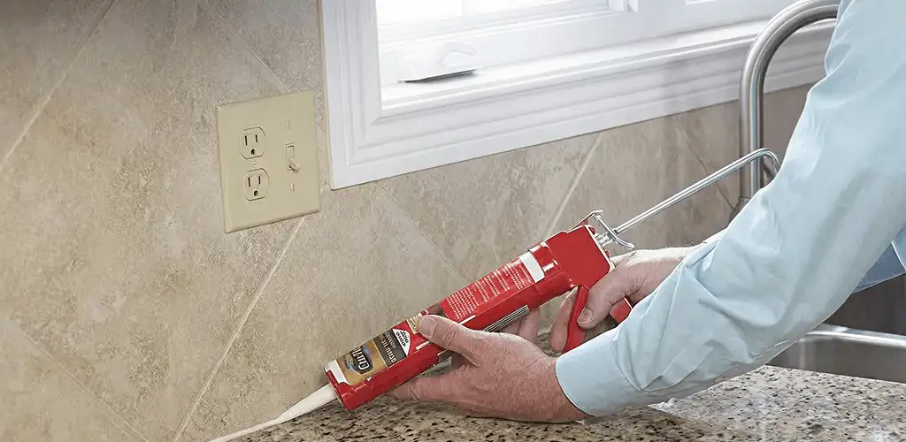 Handyman applying caulk along a kitchen backsplash and countertop seam in Arvada, CO