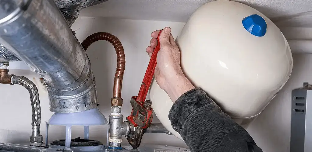 Water heater repair technician tightening plumbing connections near a tank unit in Arvada, CO